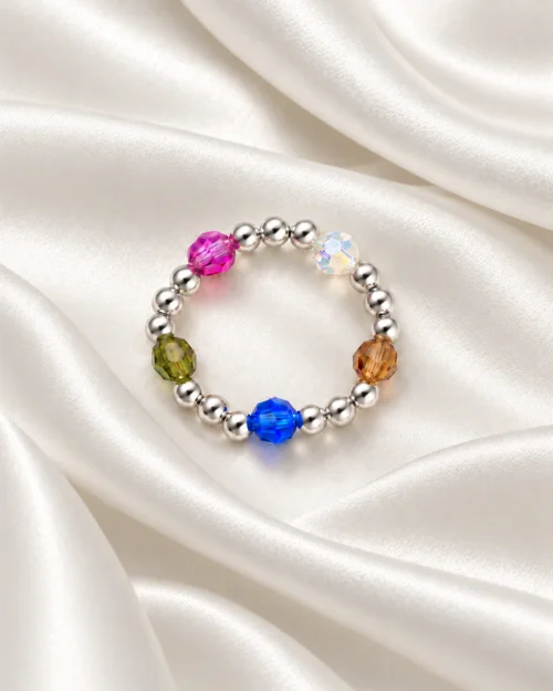 Anillo Pulso de bolas de plata de ley 925 con cristales Preciosa® de colores azul, rosa, verde, ámbar y blanco, sobre tela satinada color crema