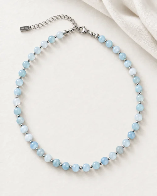 Collar Riviera de bolas de aguamarina azul claro y detalles de plata de ley 925, sobre fondo color crema con tela satinada