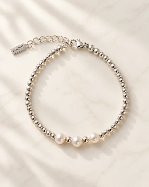 Pulsera Lua de bolas de plata de ley 925 con tres perlas naturales centrales, sobre fondo de mármol color crema
