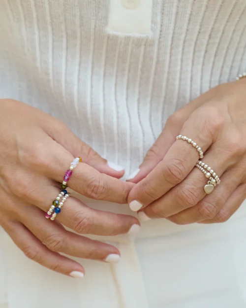 Mujer luciendo anillos de plata de ley 925 con cristales de colores en ambas manos, combinados con otros anillos de AULINE